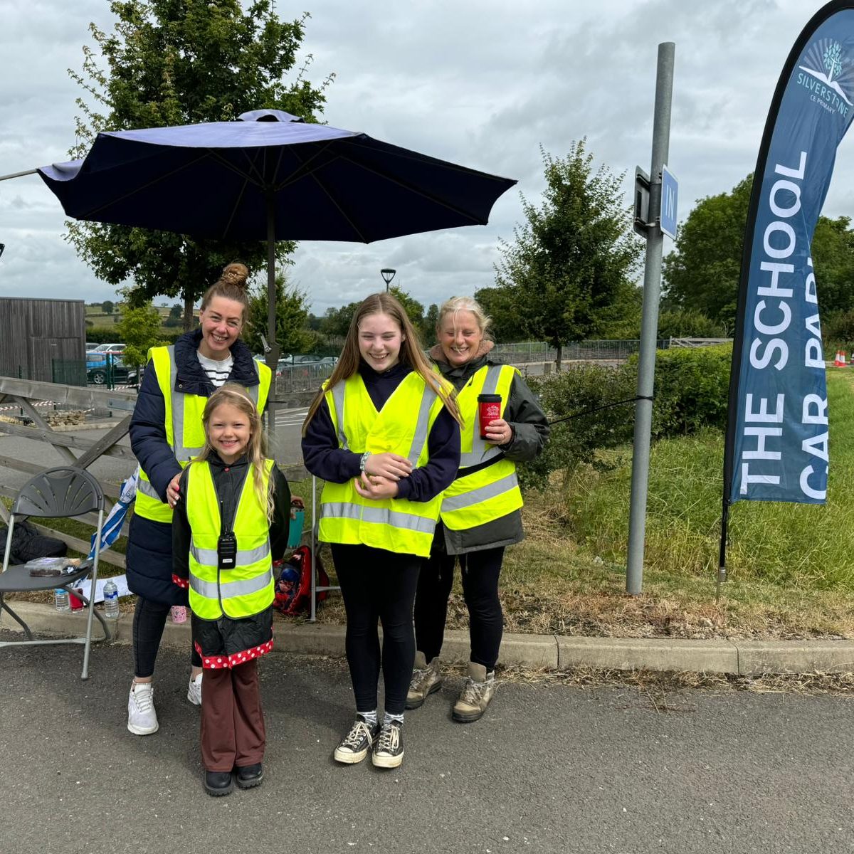 Volunteers smiling next to flag saying "The School Car Park"